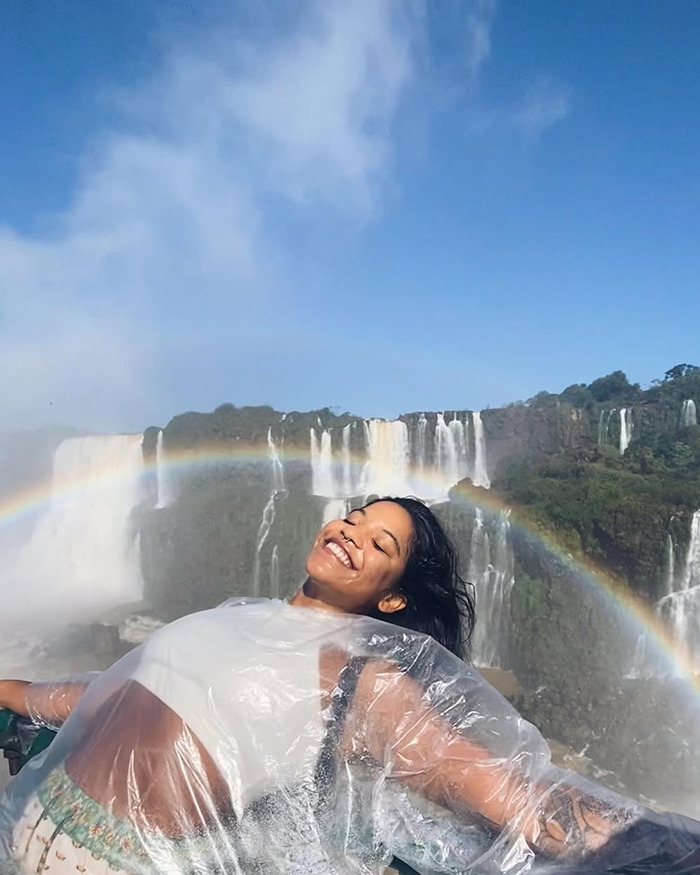 Tourist smiling near waterfall with rainbow, highlighting outrage after viral final post from active volcano incident. Tourist smiling near waterfall with rainbow, highlighting outrage after viral final post from active volcano incident.