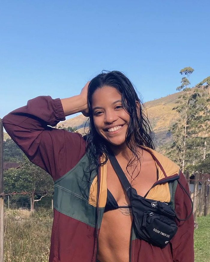 Young tourist smiling outdoors wearing a maroon jacket and black bikini top with hills in the background. Young tourist smiling outdoors wearing a maroon jacket and black bikini top with hills in the background.