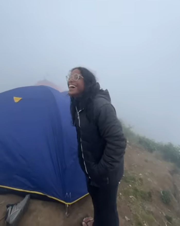 Young tourist smiling near a blue tent in foggy conditions on an active volcano, capturing a final viral moment. Young tourist smiling near a blue tent in foggy conditions on an active volcano, capturing a final viral moment.