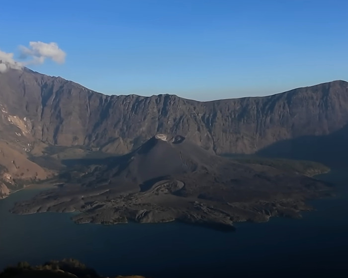 Aerial view of an active volcano surrounded by a crater lake under clear blue sky, highlighting volcanic terrain and rocky cliffs. Aerial view of an active volcano surrounded by a crater lake under clear blue sky, highlighting volcanic terrain and rocky cliffs.