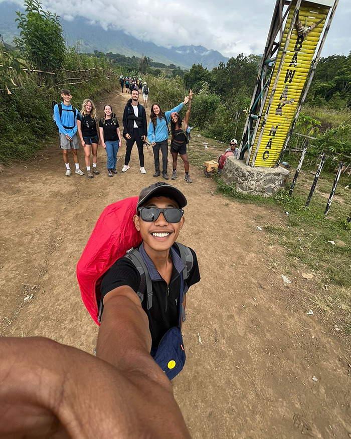 Young tourist taking a selfie with a group on a hiking trail near an active volcano, capturing the moment outdoors. Young tourist taking a selfie with a group on a hiking trail near an active volcano, capturing the moment outdoors.