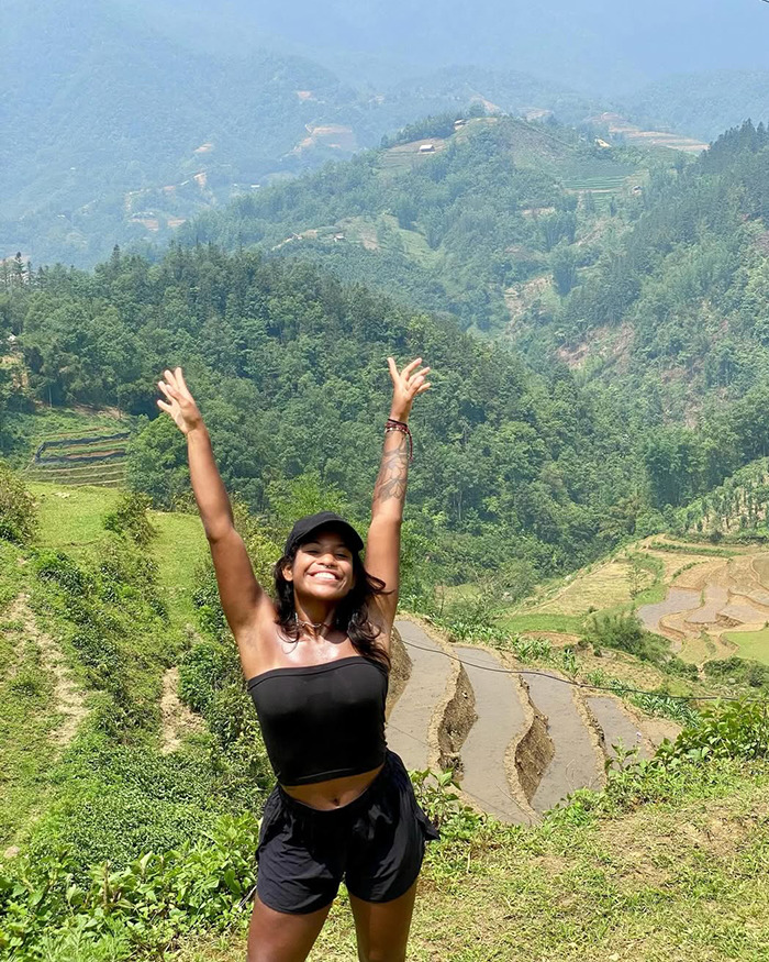 Smiling woman in black outfit raising hands with terraced fields and green mountains in background on a sunny day. Smiling woman in black outfit raising hands with terraced fields and green mountains in background on a sunny day.