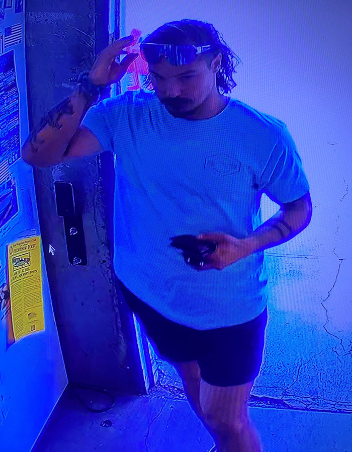 Man in blue shirt and shorts adjusting sunglasses, captured in a surveillance image related to Travis Decker neighbor encounter.