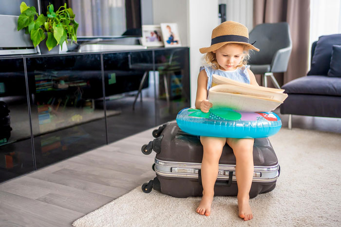 Young child sitting on suitcase with float ring, reading a book indoors, representing vacation without kids babysitting. Young child sitting on suitcase with float ring, reading a book indoors, representing vacation without kids babysitting.