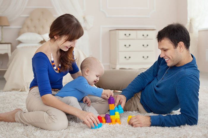Young parents playing with their baby on the floor, illustrating vacation without kids babysitting and family time at home.