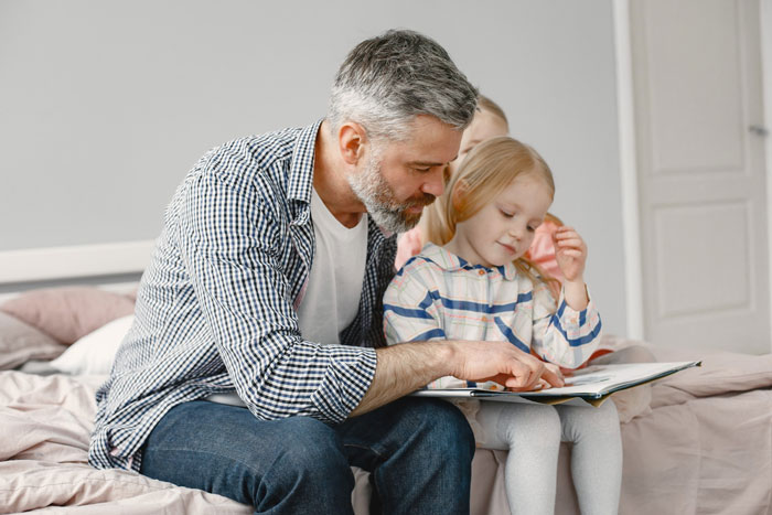 Man reading a book with daughter on bed, highlighting quality time during vacation without kids babysitting arrangements. Man reading a book with daughter on bed, highlighting quality time during vacation without kids babysitting arrangements.