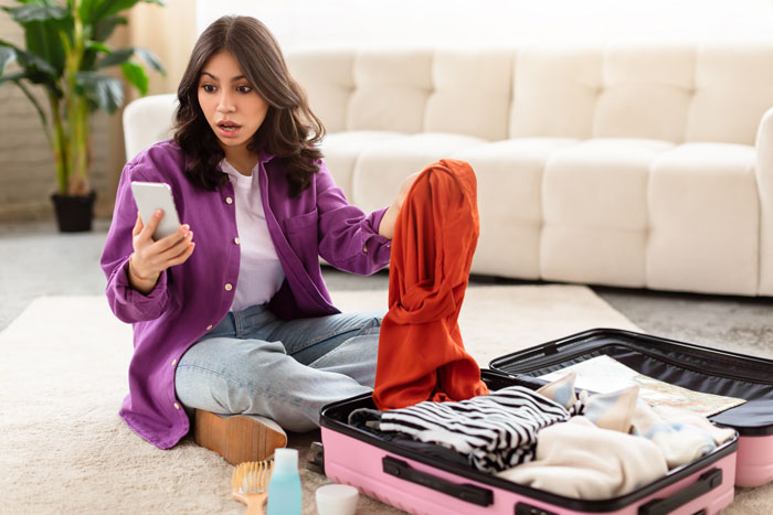 Young woman packing suitcase and checking phone, preparing for vacation without kids babysitting arrangements at home. Young woman packing suitcase and checking phone, preparing for vacation without kids babysitting arrangements at home.