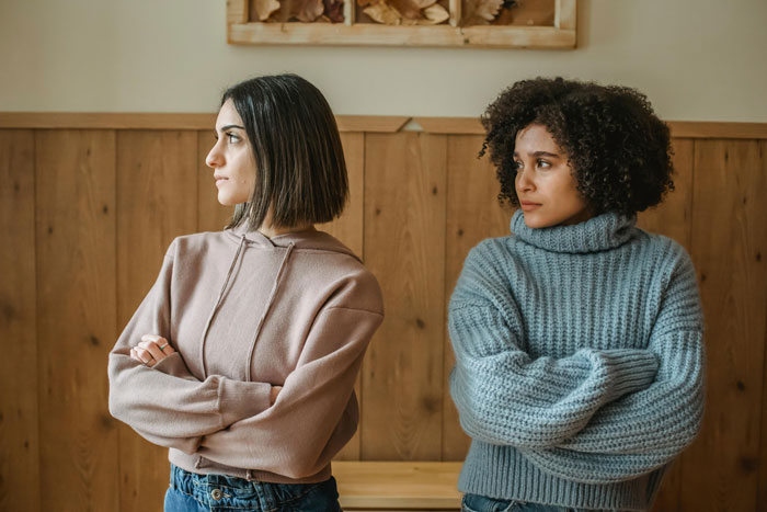 Two women with crossed arms looking away, expressing tension during a vacation without kids babysitting discussion.