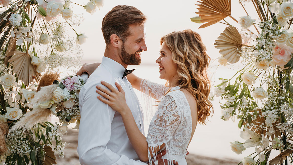 Bride and groom smiling and embracing during wedding ceremony with floral decorations and shocked wedding guests nearby