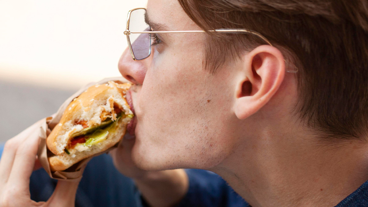 Young man wearing glasses eating a sandwich, capturing a moment that feels like another dimension on public transport.