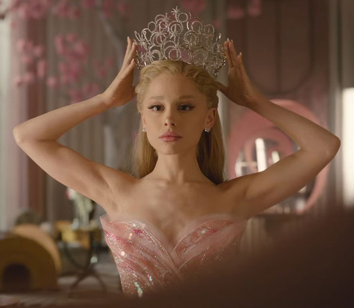 Ariana Grande wearing a sparkling pink gown and crown, showcasing an entirely visible ribcage in a dramatic scene. Ariana Grande wearing a sparkling pink gown and crown, showcasing an entirely visible ribcage in a dramatic scene.