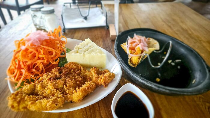 Plate with fried chicken, mashed potatoes, and shredded carrots served with dipping sauce on a wooden table.