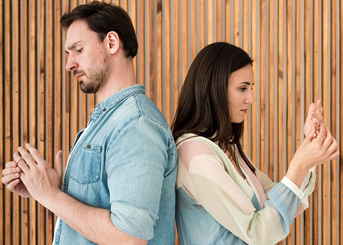 Couple standing back to back, looking upset, illustrating tension around being a tradwife in a modern relationship. Couple standing back to back, looking upset, illustrating tension around being a tradwife in a modern relationship.