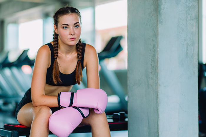 Young woman with pink boxing gloves sitting in gym, focused and determined, related to gym stalker incident story. Young woman with pink boxing gloves sitting in gym, focused and determined, related to gym stalker incident story.