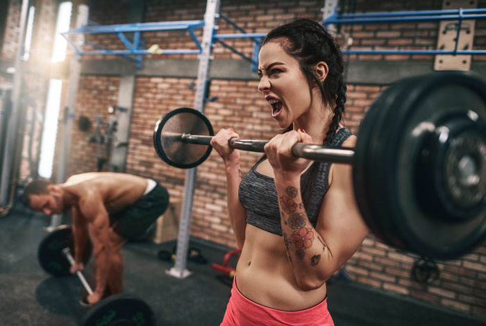 Woman lifting weights in a gym with intense focus while a man avoids unwanted attention nearby. Woman lifting weights in a gym with intense focus while a man avoids unwanted attention nearby.