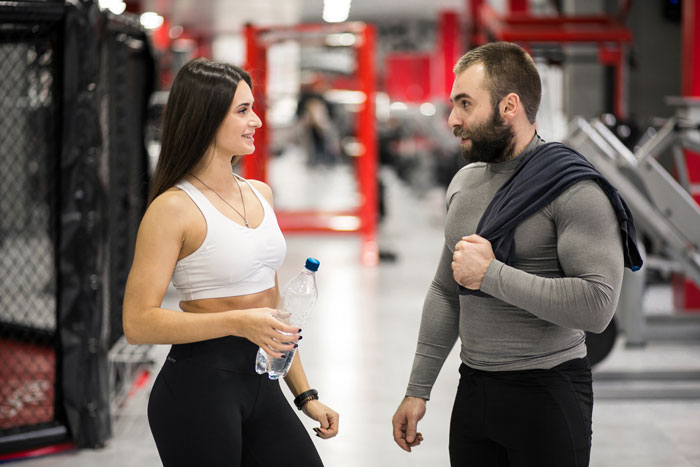 Man and woman in gym setting, man avoiding gym stalker as she flirts while holding a water bottle. Man and woman in gym setting, man avoiding gym stalker as she flirts while holding a water bottle.