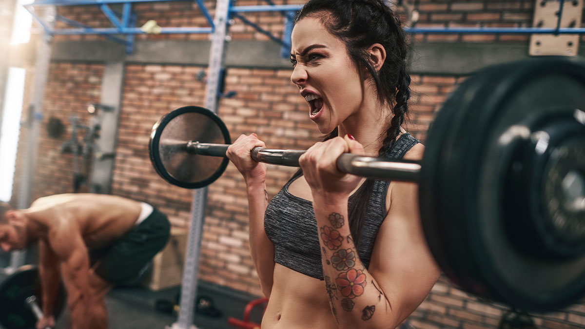 Woman lifting barbell angrily in gym, highlighting tense moment involving gym stalker and intense weights workout.
