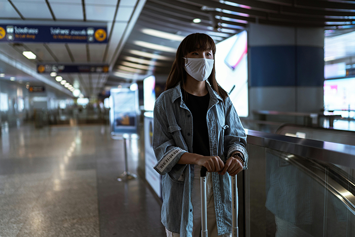 Woman move Alaska alone, standing at an airport with a suitcase, wearing a face mask and casual denim jacket, ready to travel. Woman move Alaska alone, standing at an airport with a suitcase, wearing a face mask and casual denim jacket, ready to travel.