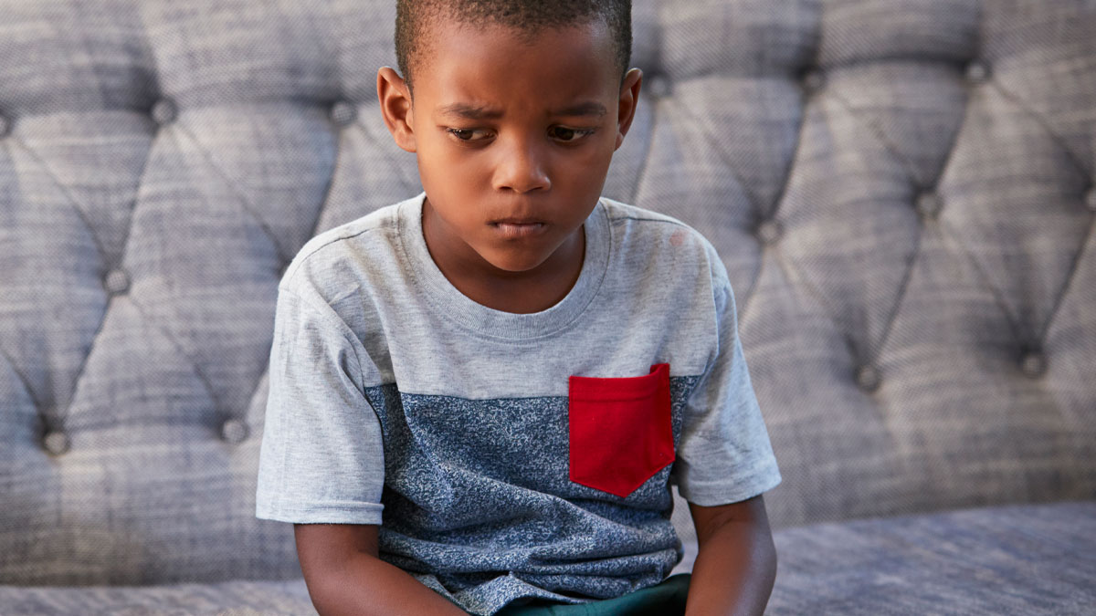 Young boy looking upset and sitting on a couch illustrating babysitter and discrimination concerns.