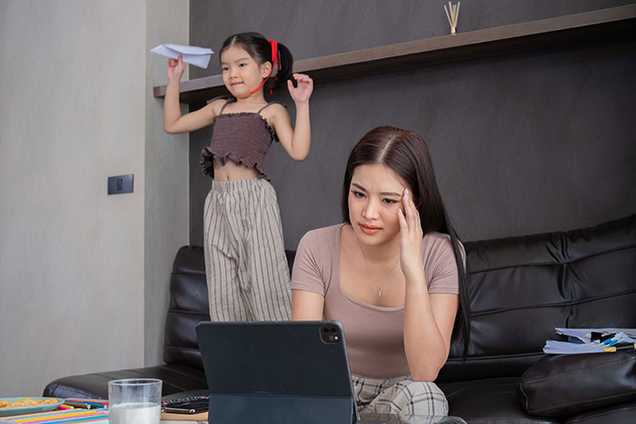 Young woman looking upset while seated on a couch with a child playing in the background, highlighting family conflict. Young woman looking upset while seated on a couch with a child playing in the background, highlighting family conflict.