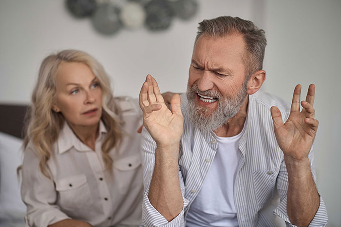 Middle-aged man expressing frustration while woman looks on, illustrating confrontation and breakup themes. Middle-aged man expressing frustration while woman looks on, illustrating confrontation and breakup themes.