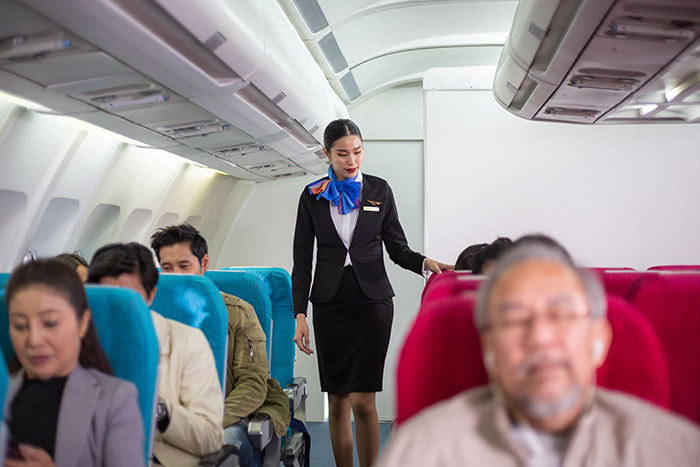 Flight attendant walking down airplane aisle between seated passengers, highlighting airplane seat switch and children issues. Flight attendant walking down airplane aisle between seated passengers, highlighting airplane seat switch and children issues.