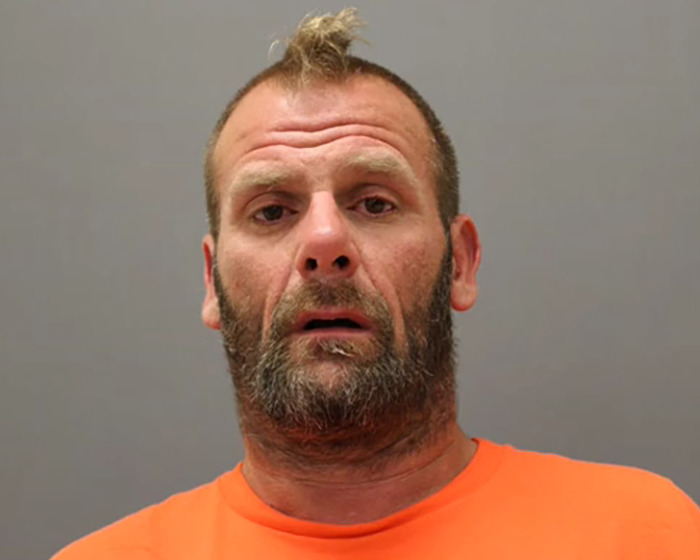 Mugshot of a man with a beard and orange shirt, related to alleged attacker in caring mother jaw injury case. Mugshot of a man with a beard and orange shirt, related to alleged attacker in caring mother jaw injury case.