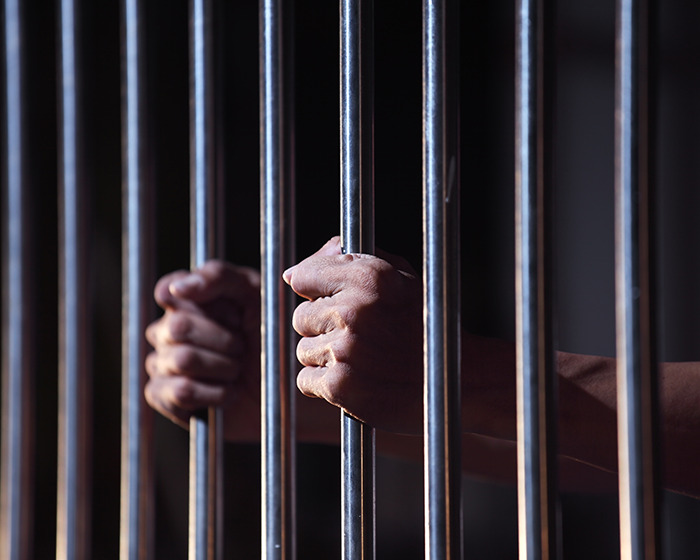 Hands gripping metal jail bars in a dark setting representing alleged attacker in a caring mother’s tragic case. Hands gripping metal jail bars in a dark setting representing alleged attacker in a caring mother’s tragic case.