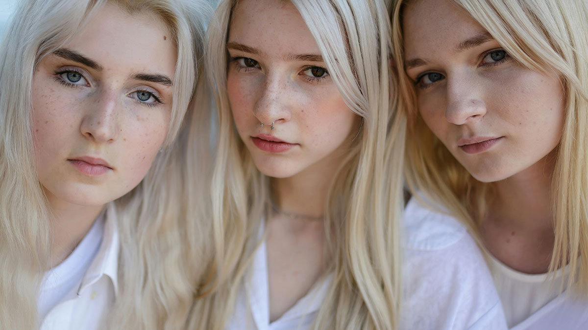 Three blonde adolescent triplets with serious expressions, representing family favoring matching triplets over the other sibling.