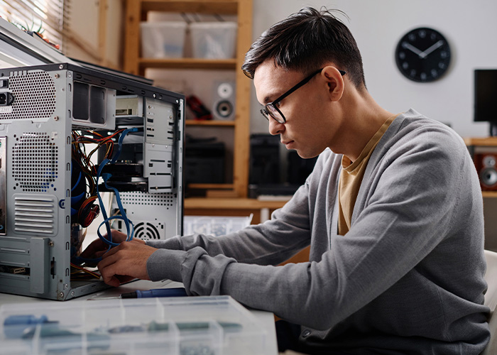 Young man repairing computer hardware, focused and working carefully on internal components at desk.