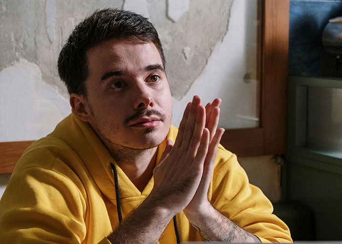 Young man in a yellow hoodie thoughtfully clasping hands, illustrating guy asks ex to move out after breakup concern. Young man in a yellow hoodie thoughtfully clasping hands, illustrating guy asks ex to move out after breakup concern.