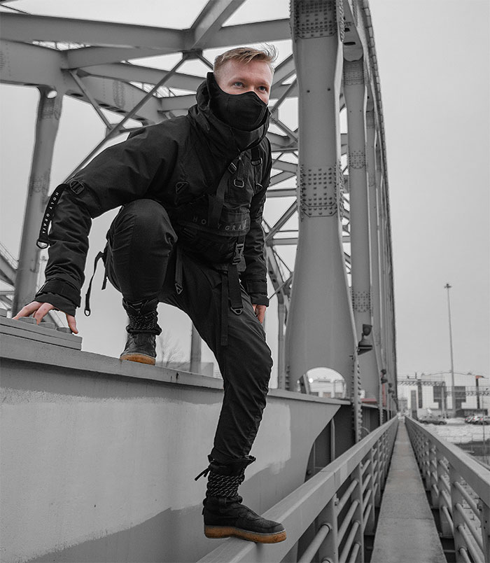 Young man dressed in black streetwear and mask climbing on bridge railing, capturing boomer complains about stranger’s pants concept. Young man dressed in black streetwear and mask climbing on bridge railing, capturing boomer complains about stranger’s pants concept.