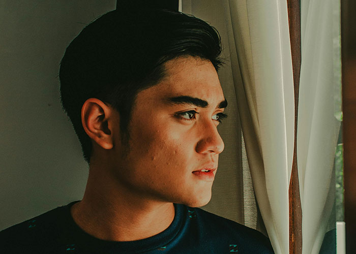 Young man looking out window with concerned expression, possibly upset about a neighbor's farm stand dispute. Young man looking out window with concerned expression, possibly upset about a neighbor's farm stand dispute.