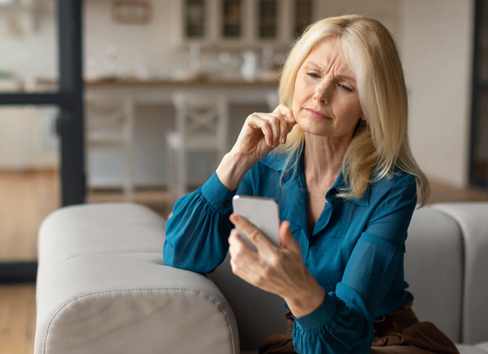 Woman using mil-tracking-app-son on smartphone, sitting on couch in home, looking thoughtful while checking device. Woman using mil-tracking-app-son on smartphone, sitting on couch in home, looking thoughtful while checking device.