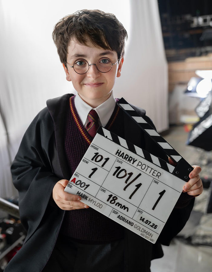 Young actor dressed as Harry Potter holding a clapperboard on the set of HBO's upcoming Harry Potter show. Young actor dressed as Harry Potter holding a clapperboard on the set of HBO's upcoming Harry Potter show.