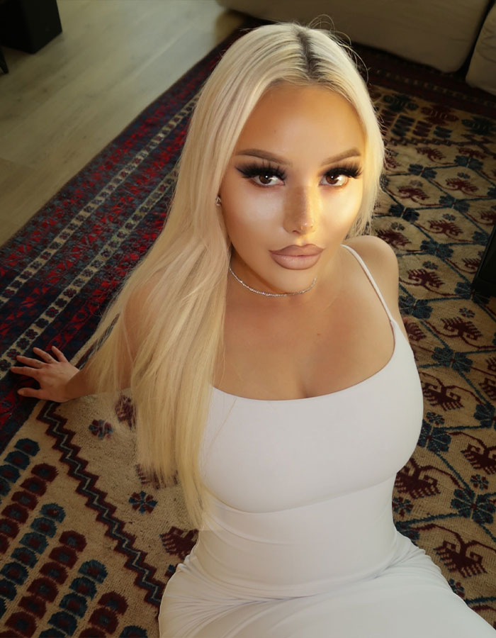 Young woman in white dress sitting indoors on patterned rug, relating to adult industry mental health and substance issues. Young woman in white dress sitting indoors on patterned rug, relating to adult industry mental health and substance issues.