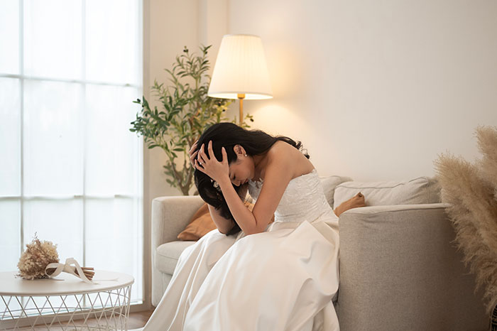 Bride in a white dress sitting on a neutral-toned couch looking upset in a softly lit living room setting. Bride in a white dress sitting on a neutral-toned couch looking upset in a softly lit living room setting.