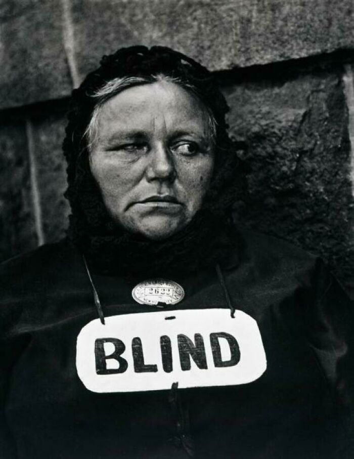 Somber historic photo of a blind woman wearing a marked sign, capturing a gut-wrenching moment from history.