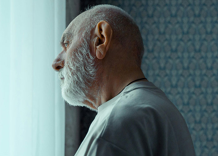 Elderly man with a white beard looking pensively out a window in a dimly lit room reflecting on a difficult relationship. Elderly man with a white beard looking pensively out a window in a dimly lit room reflecting on a difficult relationship.