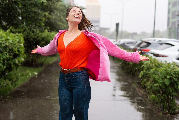 Woman enjoying rain in public, arms outstretched, wearing bright clothing, illustrating wild to disgusting public acts.