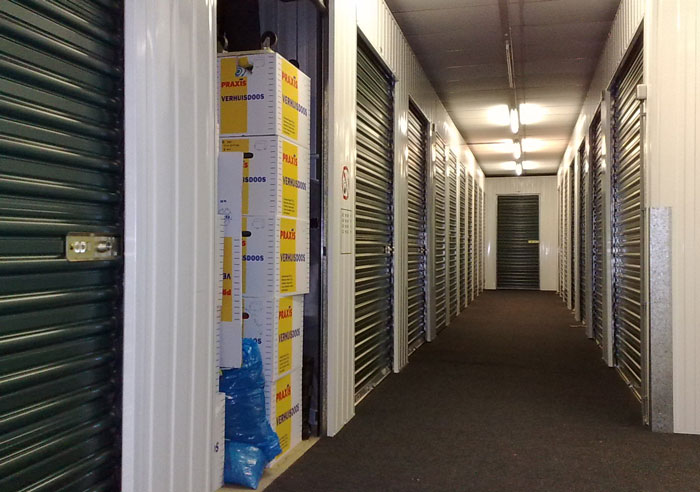 Storage unit hallway with partially open door revealing packed boxes inside, symbolizing hidden memories and family legacy.