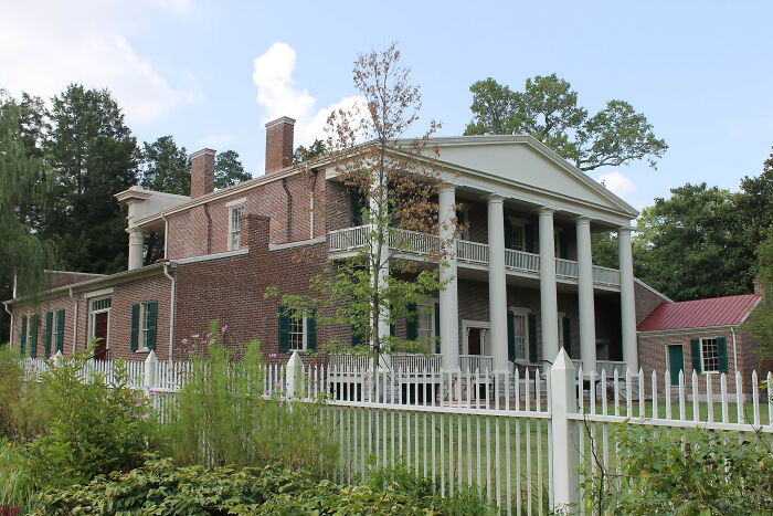Historic home with classic American architecture featuring large columns, brick walls, and a white picket fence.