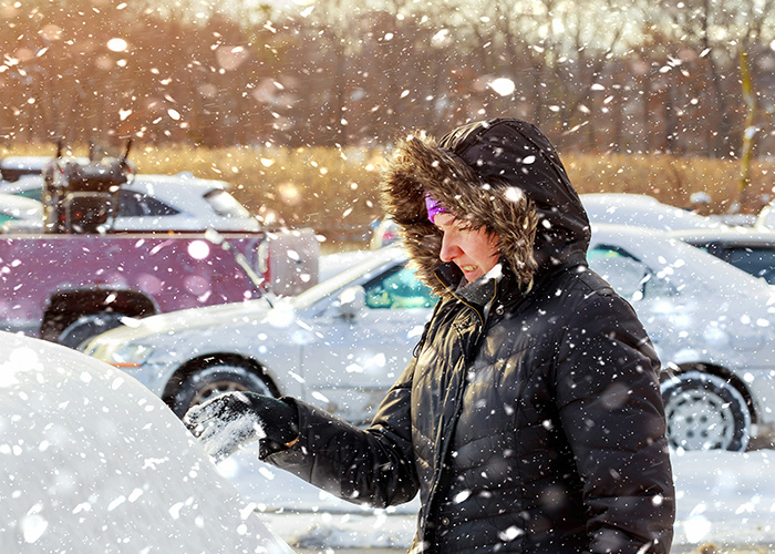 Person in a black winter coat brushing snow off a car during heavy snowfall, illustrating facts people are tired of explaining.