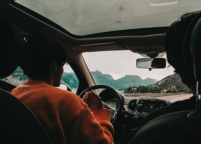 Two people inside a car driving through mountainous landscape, illustrating bizarre family habits thought normal.