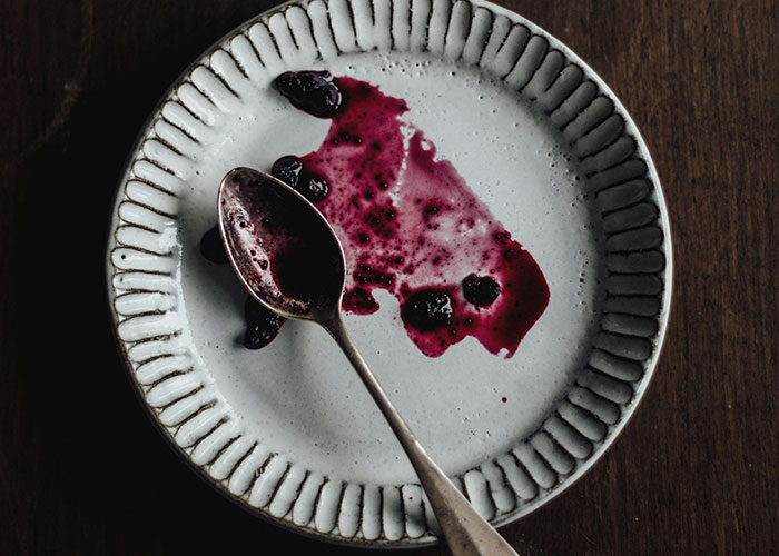 Empty plate with remnants of dark berry sauce and a spoon, illustrating bizarre family food habits thought normal.