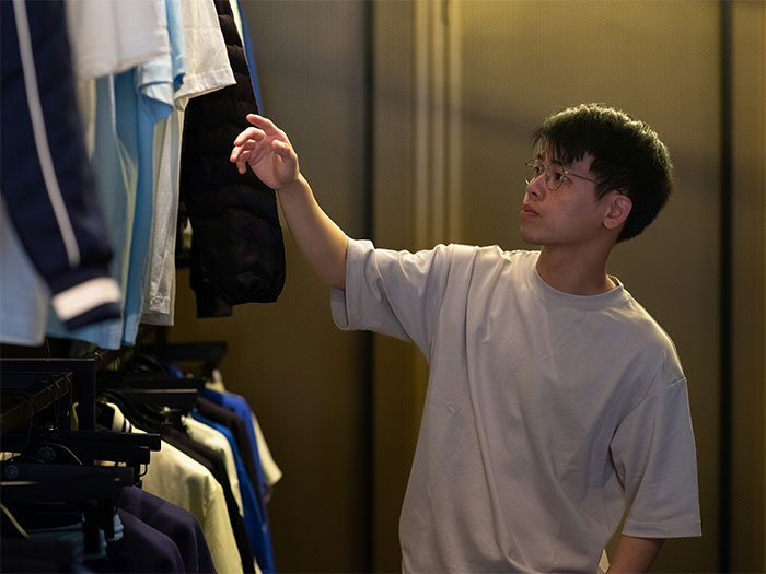 Young man browsing clothes in dimly lit store, illustrating boomer complains about stranger’s pants situation. Young man browsing clothes in dimly lit store, illustrating boomer complains about stranger’s pants situation.