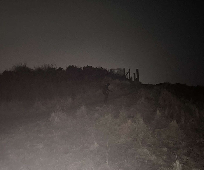 Dark night scene showing a mysterious figure in a full-body cat suit crawling on a grassy hill near a fence. Dark night scene showing a mysterious figure in a full-body cat suit crawling on a grassy hill near a fence.