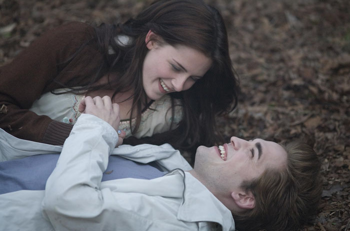 Robert Pattinson and Kristen Stewart in a Twilight intimate scene, smiling closely while lying on the forest floor. Robert Pattinson and Kristen Stewart in a Twilight intimate scene, smiling closely while lying on the forest floor.