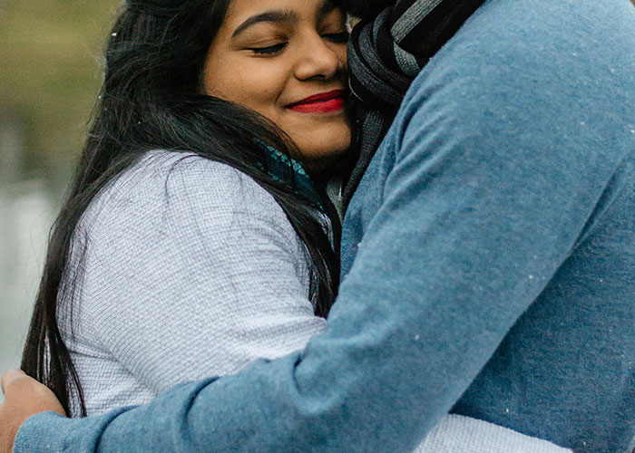 Young woman smiling with eyes closed while hugging a family member, reflecting bizarre family moments considered normal.