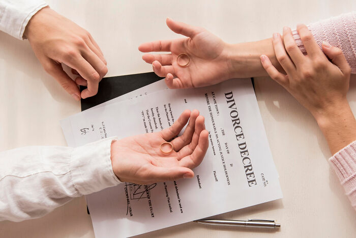 Hands holding wedding rings over a divorce decree document, illustrating signs a couple’s days are numbered.